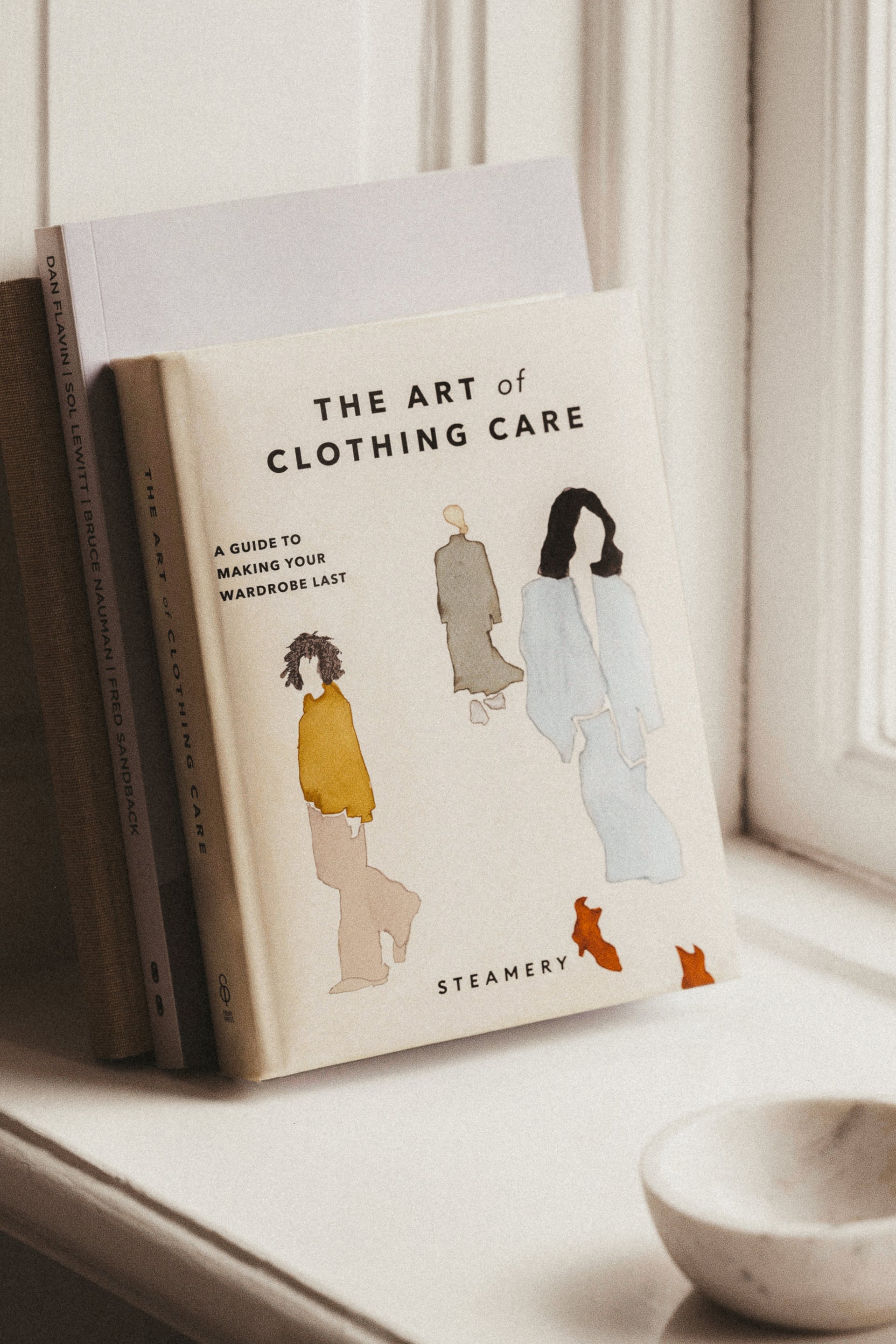 Book titled 'The Art of Clothing Care' on a windowsill with a light background