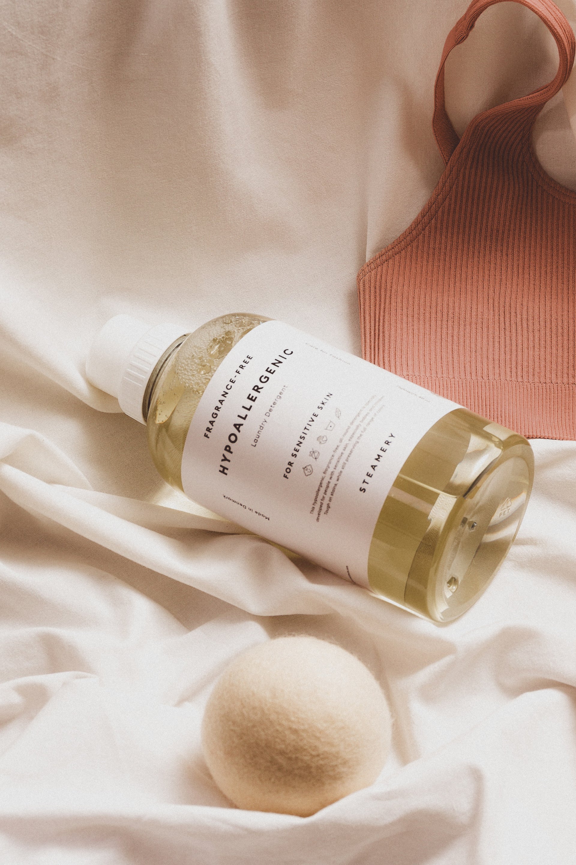 Bottle of hypoallergenic laundry detergent with a wooden ball on a soft fabric background
