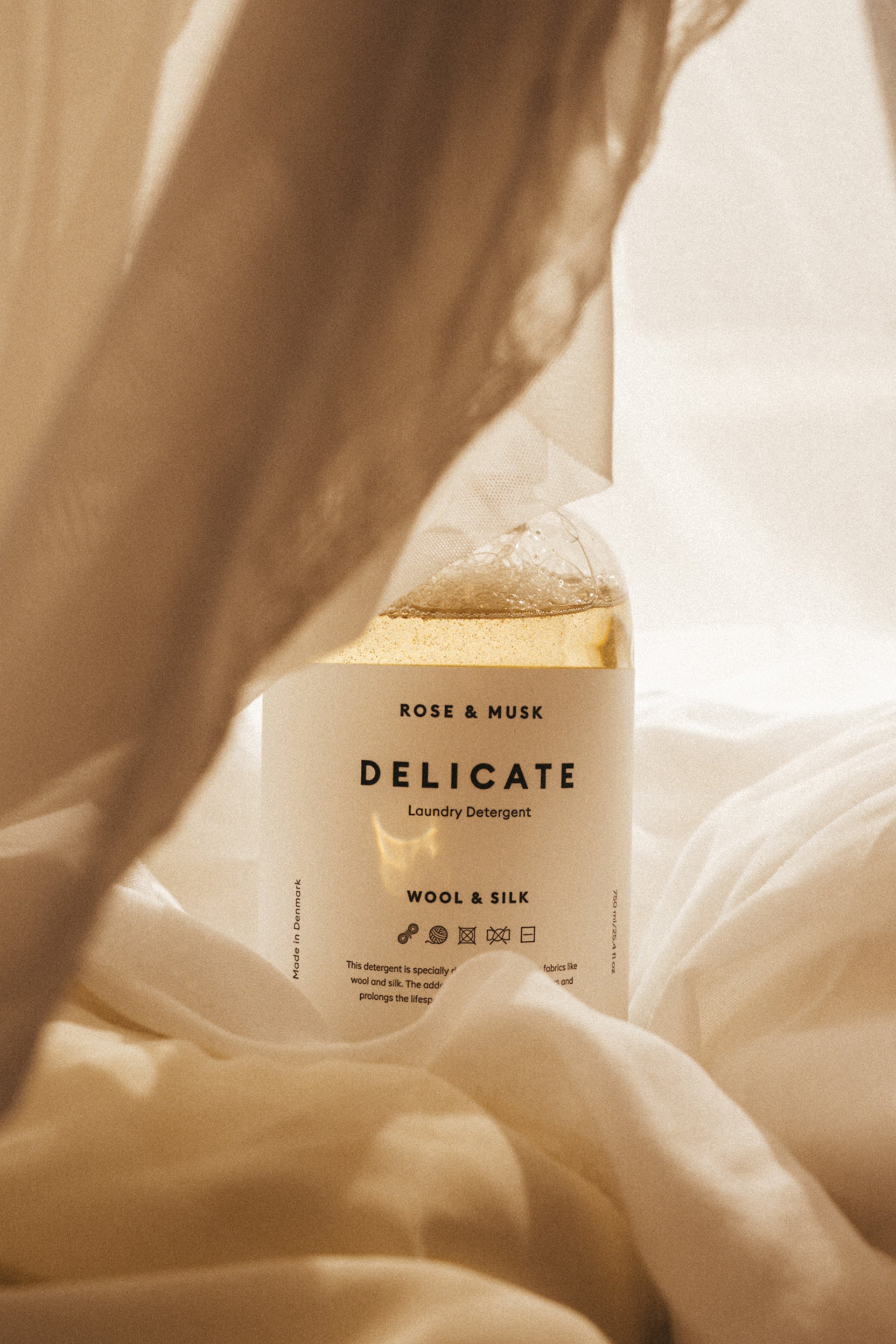 Delicate laundry detergent bottle with 'Rose & Musk' fragrance on a soft fabric background