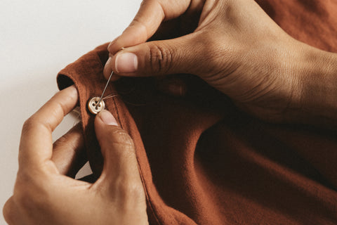 Person buttoning a brown garment with a white background