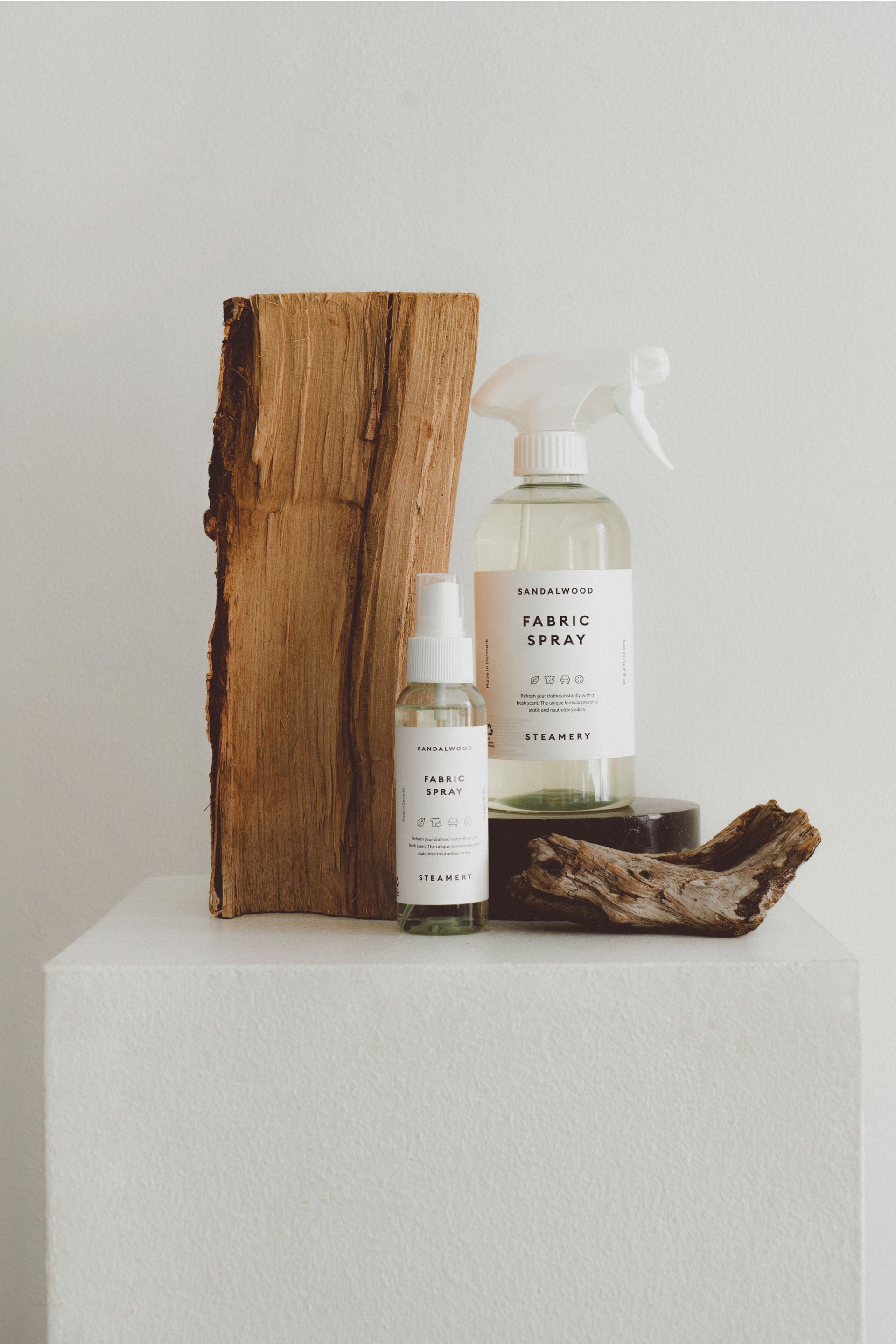 Two fabric spray bottles on a white surface with a wooden block in the background.