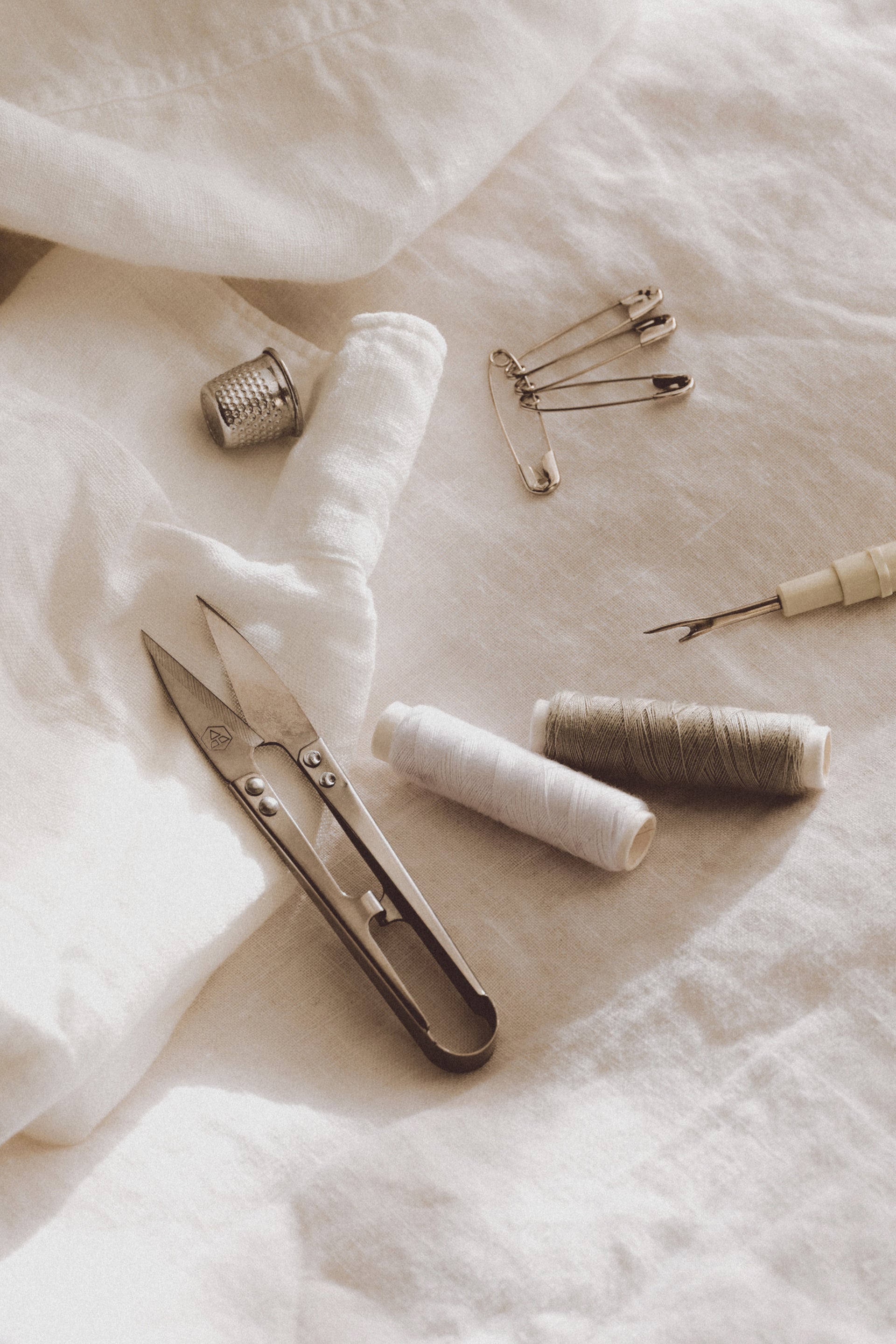 Sewing tools including a knife, thimble, safety pins, and thread on a textured fabric background.