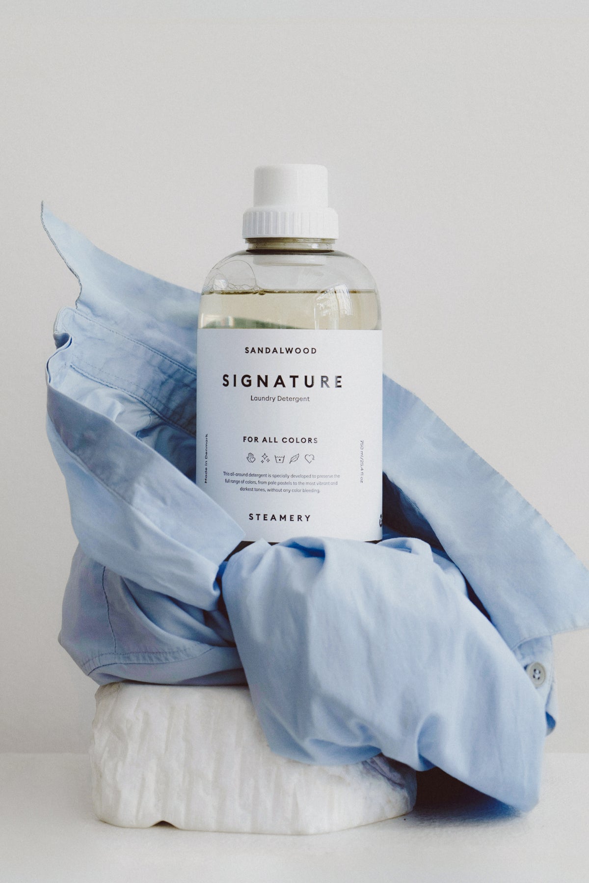 Bottle of 'Signature' laundry detergent with a blue garment on a light gray background
