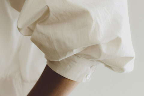 Close-up of a person wearing a white shirt with rolled-up sleeves on a light background