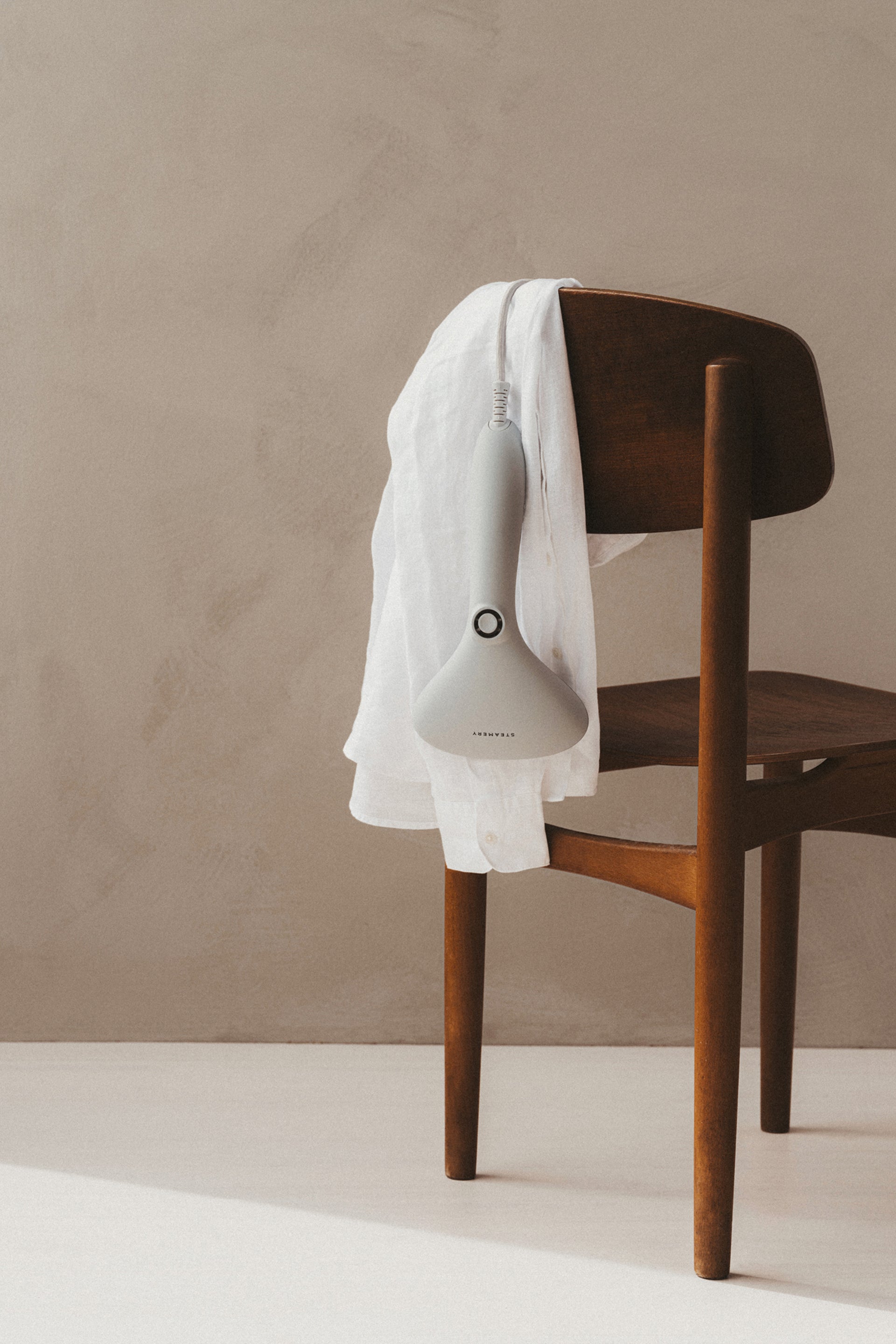 Grey handheld steamer on a wooden chair with a beige background