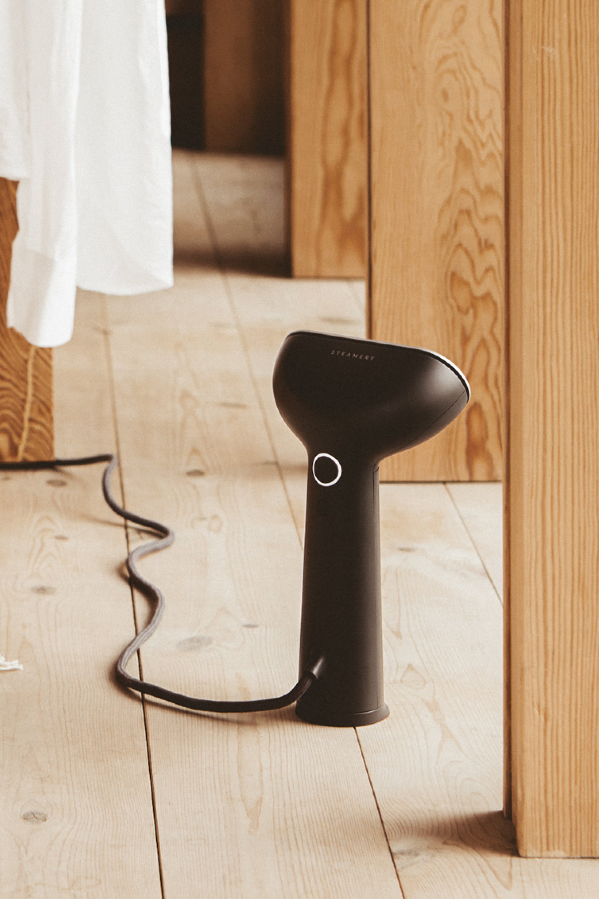 Black handheld steamer on a wooden floor with a blurred background