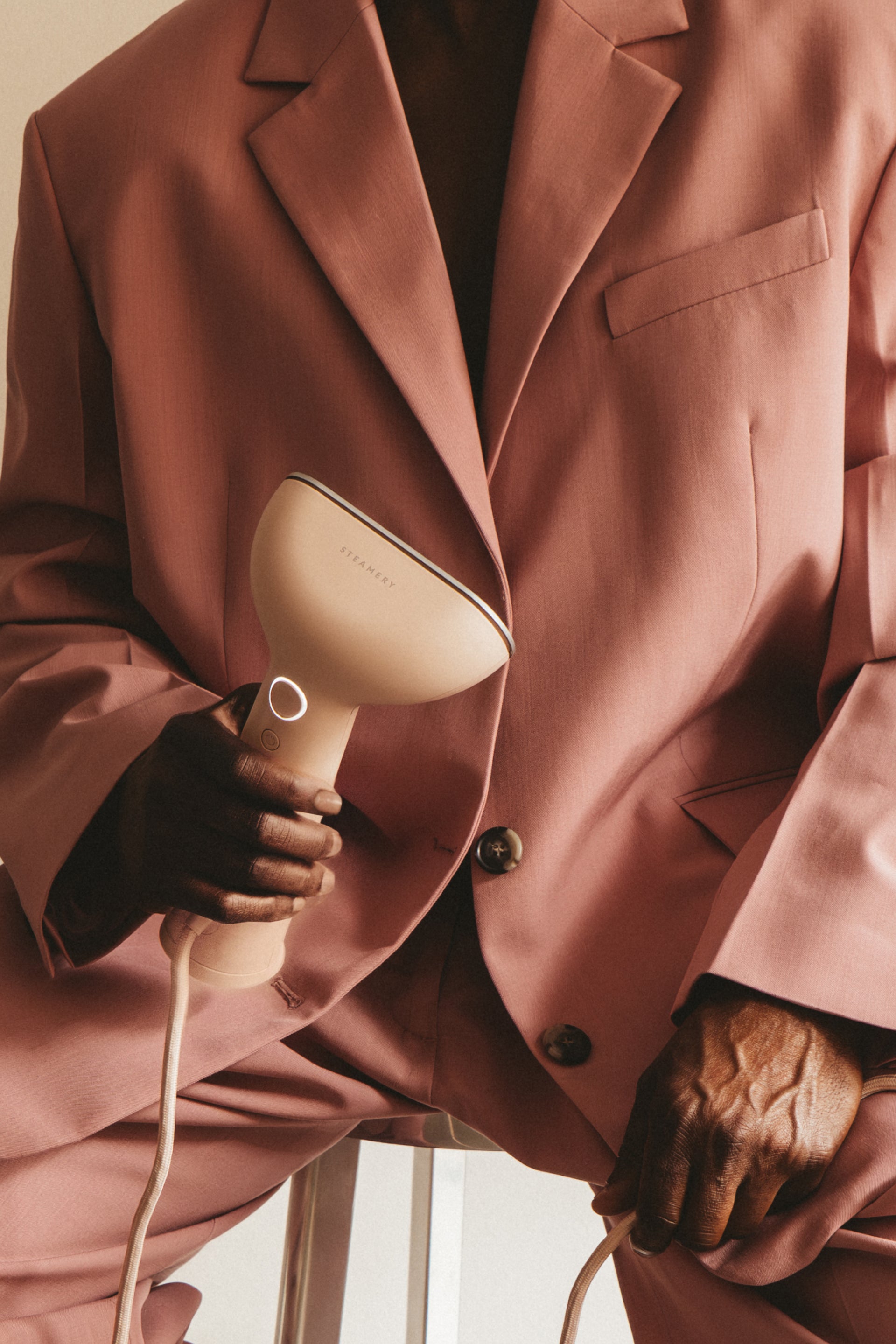 Person wearing a pink blazer holding a pink handheld steamer.