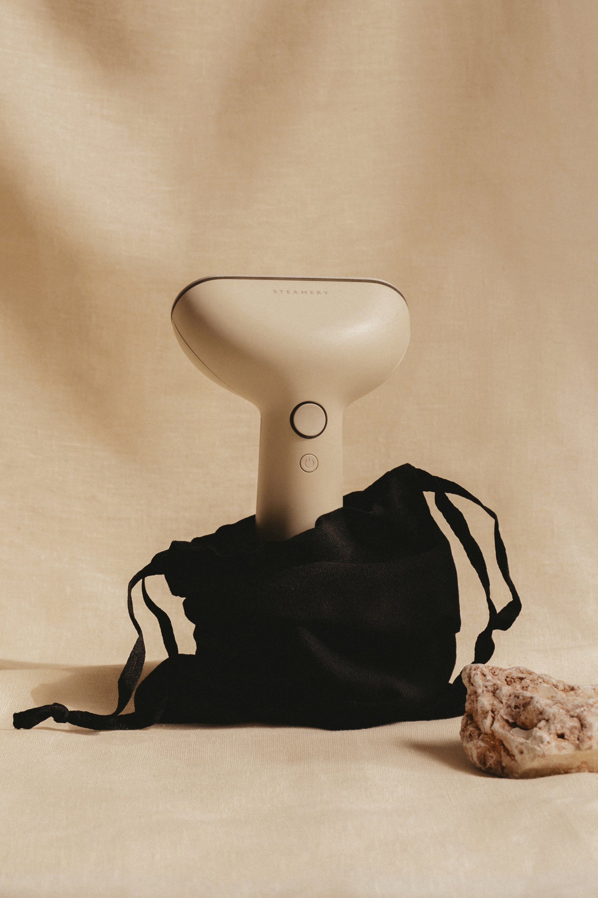 White handheld steamer with a black drawstring bag on a beige background