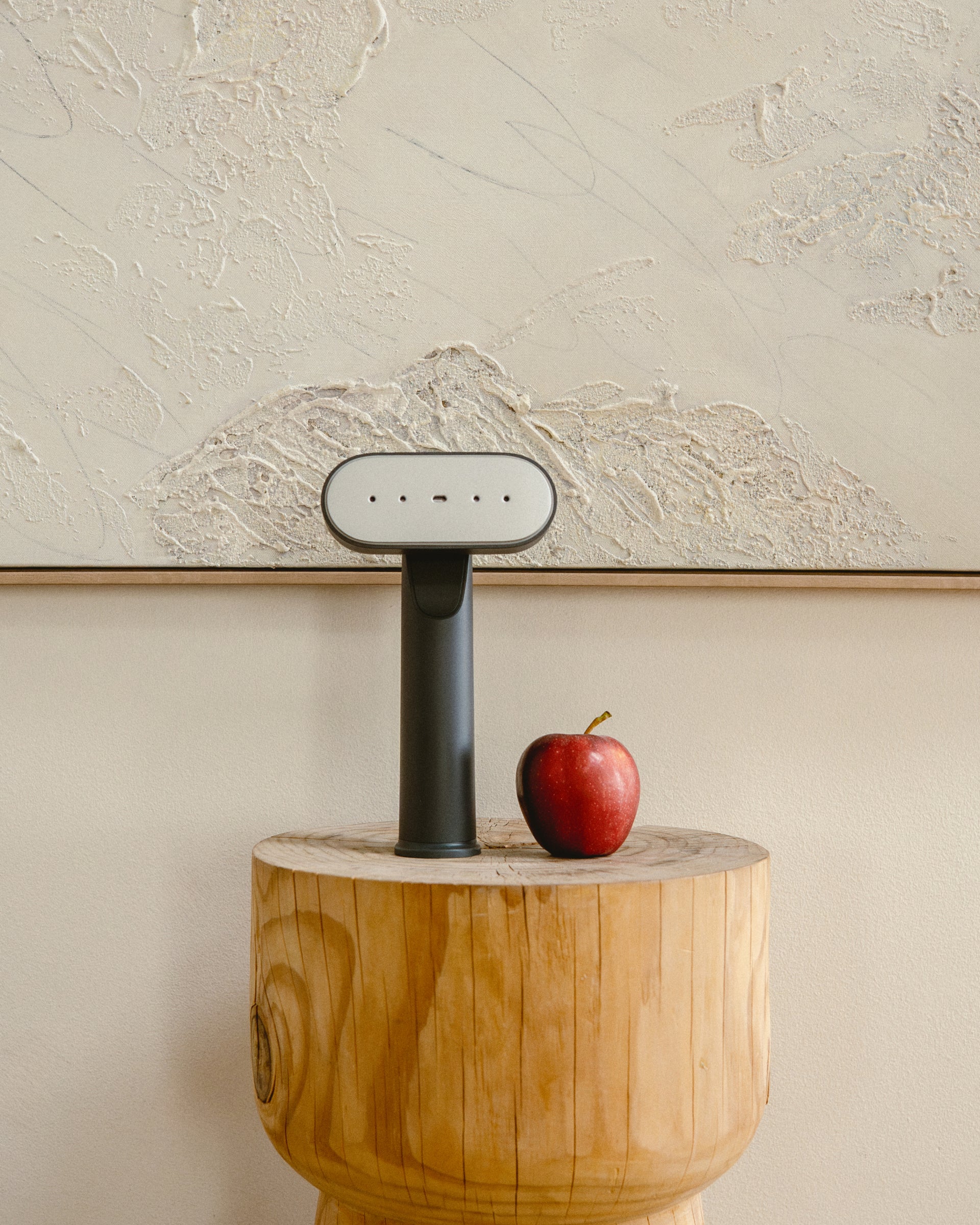 Handheld steamer on a wooden block with an apple next to it against a textured wall.