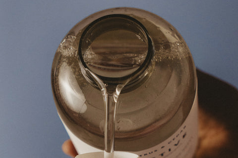 Close-up of a bottle being tilted, with detergent dripping from the cap against a blue background.