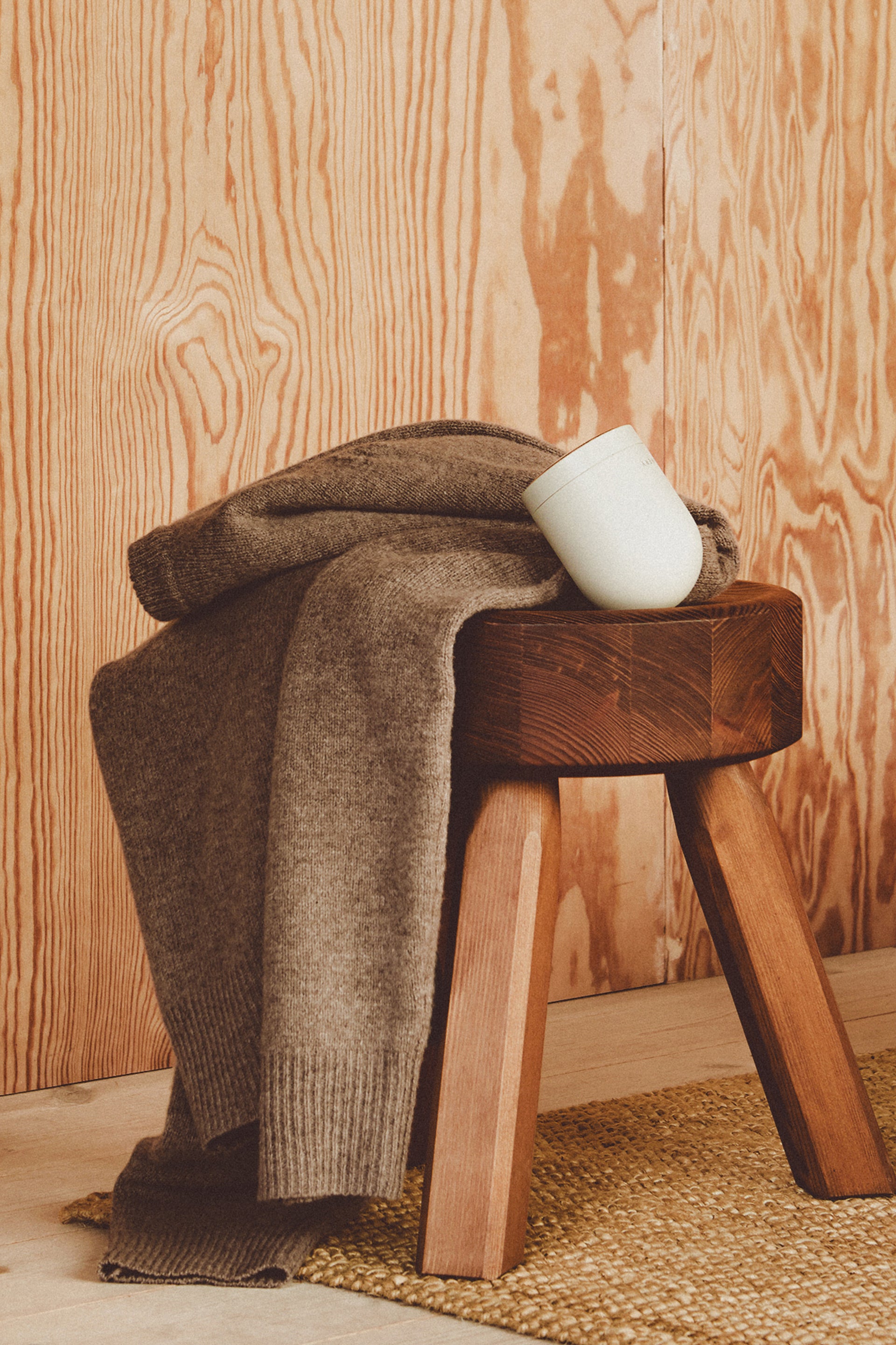 Brown sweater draped over a wooden stool with a white fabric shavers on a wooden floor.