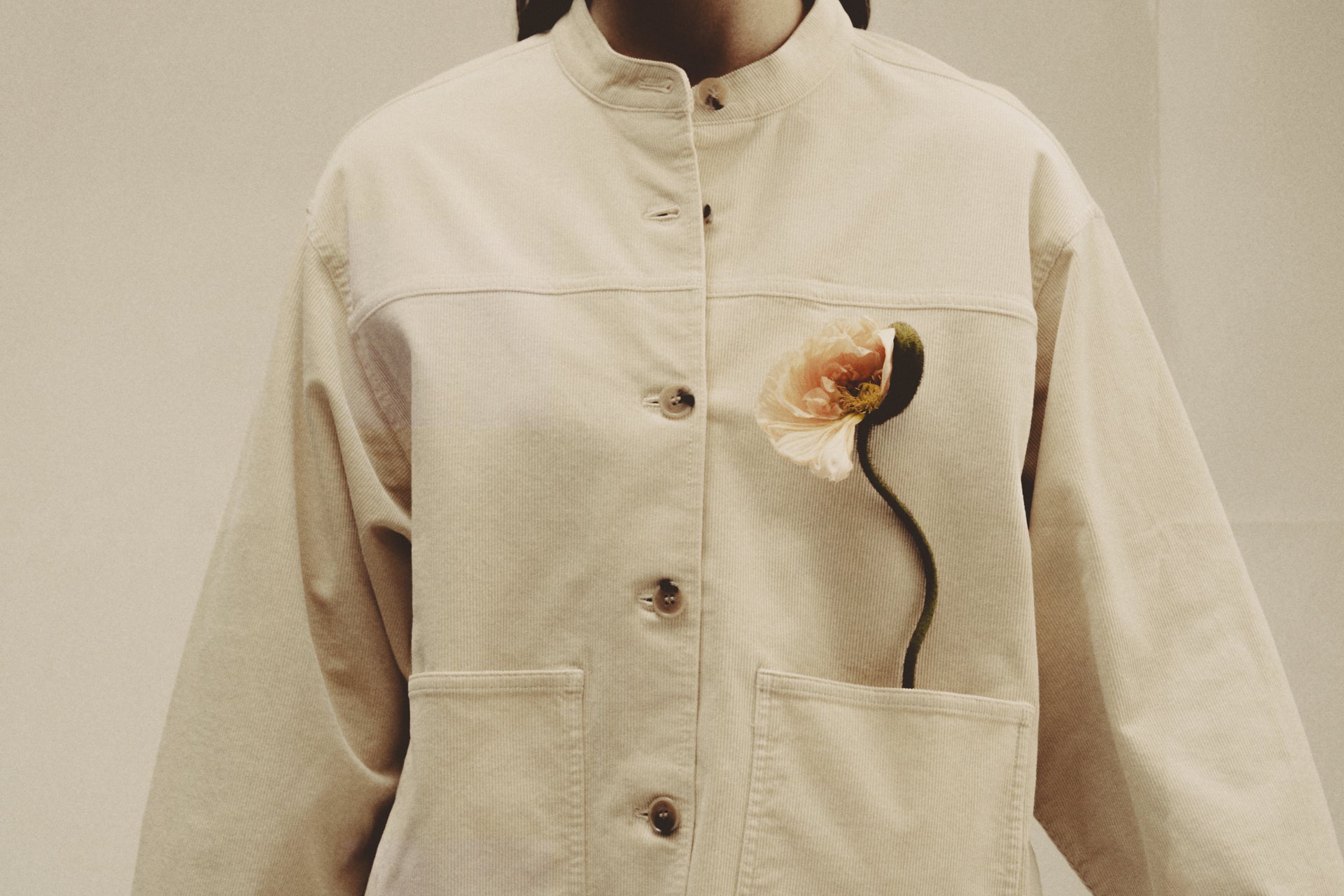 Beige jacket with a floral design on the chest against a neutral background