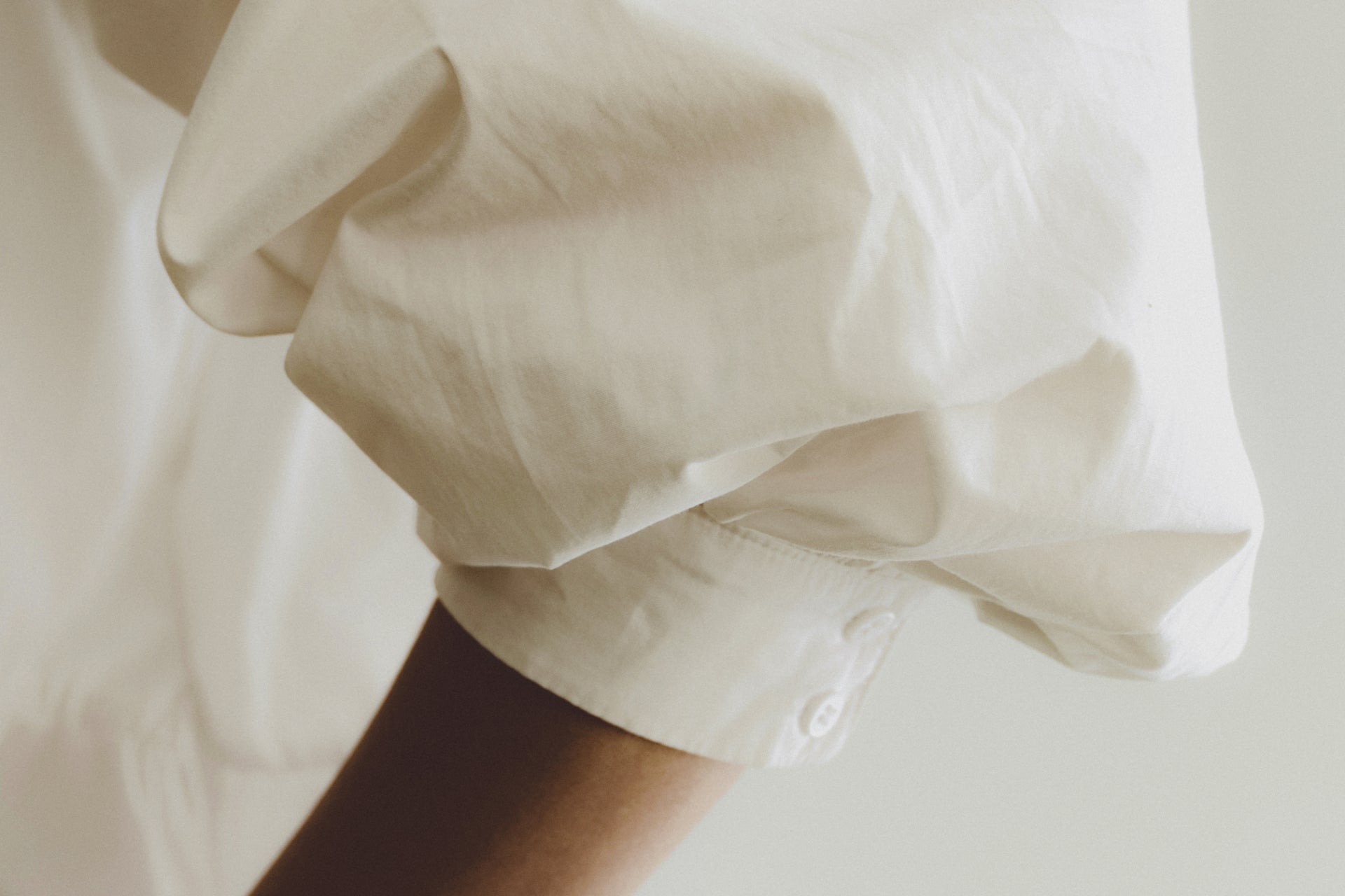 Close-up of a person wearing a white shirt with rolled-up sleeves on a light background